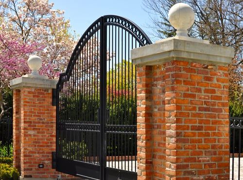 Black wrought iron driveway gate set between brick pillars