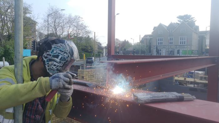 Fabricator welding a red structural steel beam on site